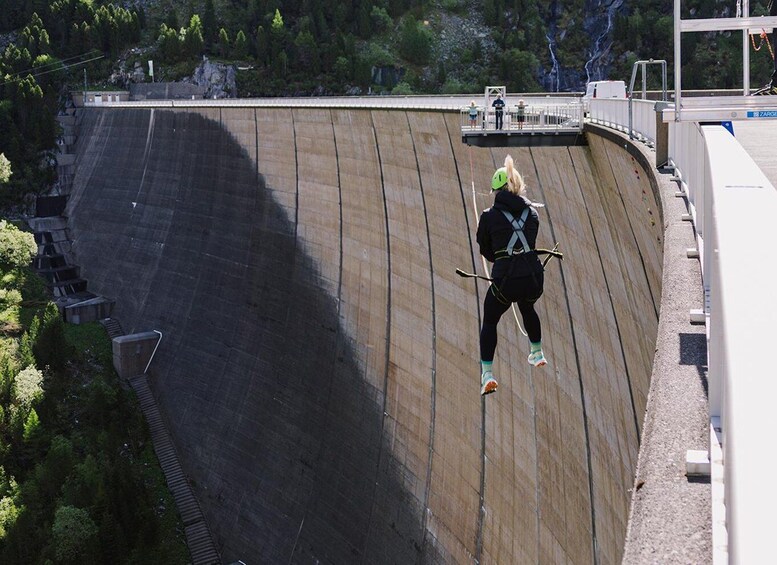 A person rappelling down a large dam with a harness and ropes. 3