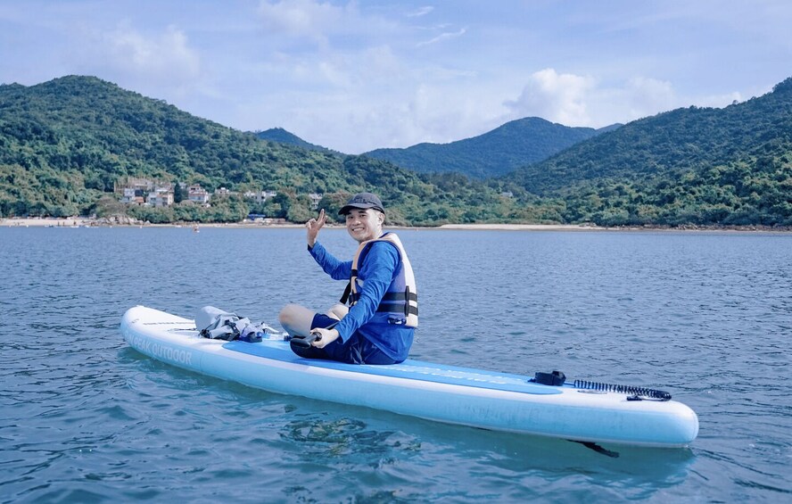 A person sitting on a blue kayak on calm water with mountains in the background. 1