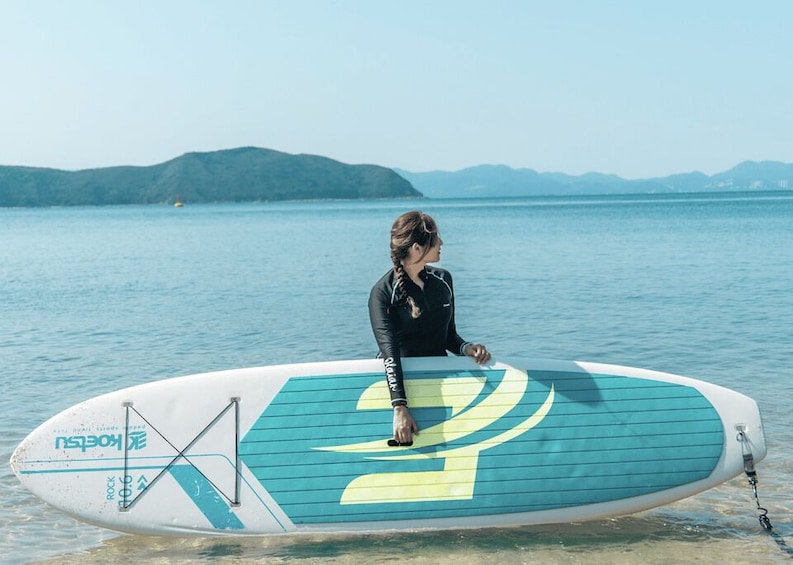 A person standing on a surfboard in calm water with mountains in the background. 2
