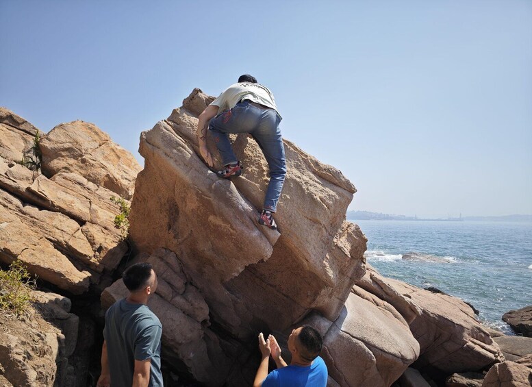 A person climbing a large rock formation near the ocean. 5