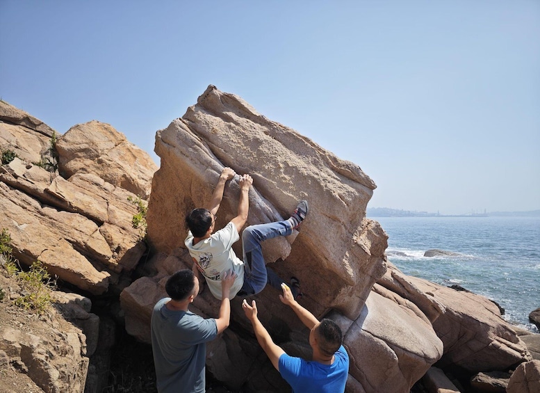 Three people climbing a large rock formation by the sea. 3