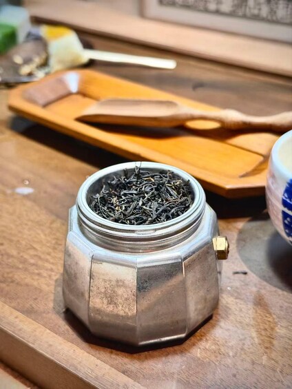 A metallic container with a hexagonal shape filled with tea leaves on a wooden surface. 5