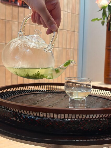 A hand pouring tea from a glass teapot into a glass cup on a tray. 4