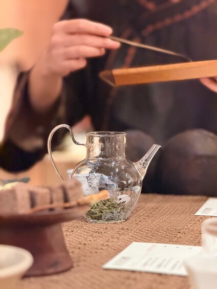 A person holding chopsticks over a glass pitcher with a tea infuser. 2