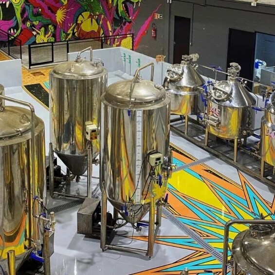 Stainless steel brewing tanks in a facility with colorful graffiti on the wall. 3