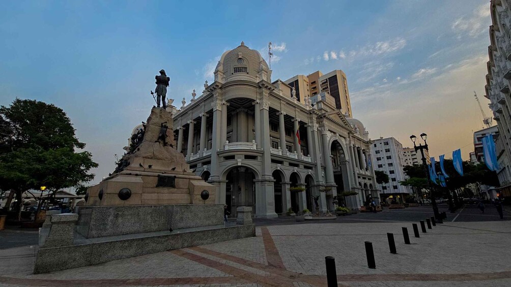 A historic building with classical architecture, a statue, and a plaza with bollards. 2