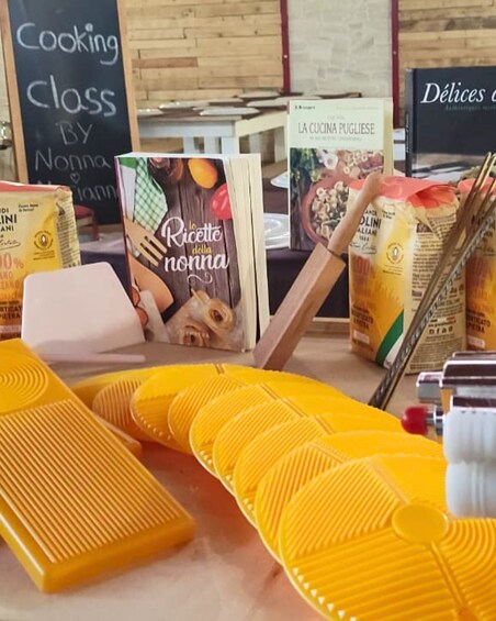 A cooking class sign, a book titled 'La Cucina Pugliese,' and yellow kitchen utensils on a table. 4