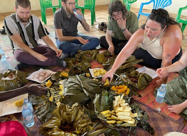 People sitting on a mat, preparing food in banana leaves. 5