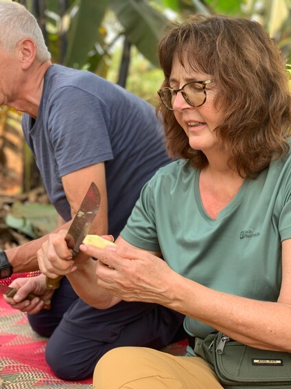 Two people sitting outdoors, one cutting a yellow fruit. 4