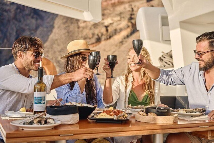 A group of people toasting with wine glasses at a table with food and a bottle of wine. 2