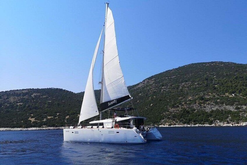 A sailboat with white sails on calm water, surrounded by a hilly landscape. 4