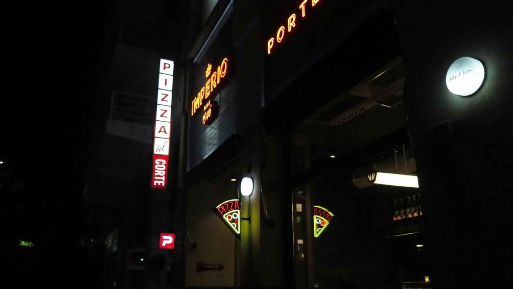 A nighttime view of a pizza restaurant with neon signs, including 'PIZZA' and 'PORTER.' 1