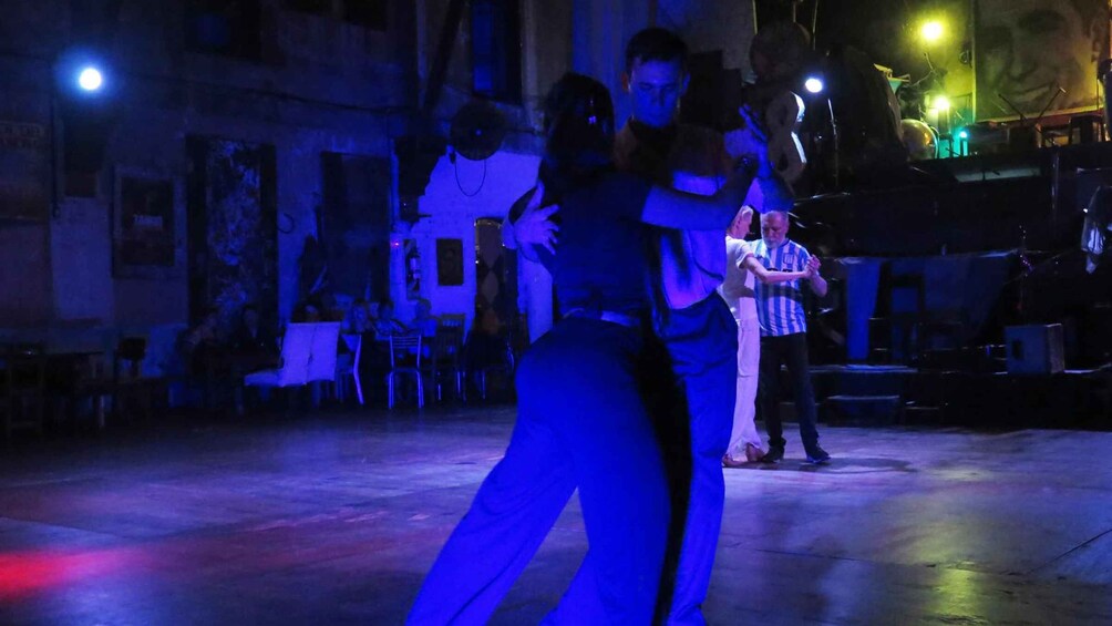 A group of people dancing in a dimly lit outdoor setting with a stage and audience in the background. 2
