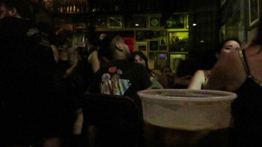 A crowded indoor setting with people, tables, and a visible trash bin. 5
