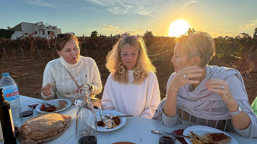 Three people dining outdoors with a vineyard in the background. 5