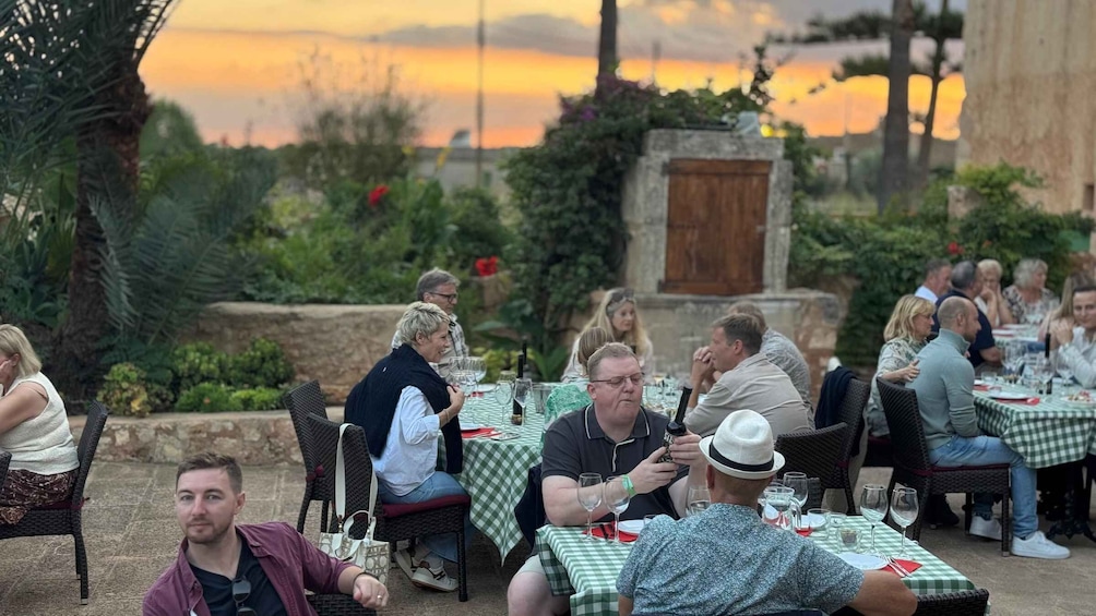 A group of people dining outdoors with a sunset in the background. 2