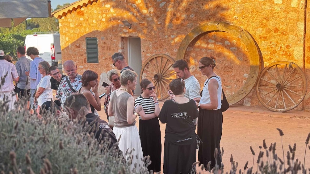 A group of people standing in front of a building with large wheels and a stone wall. 3