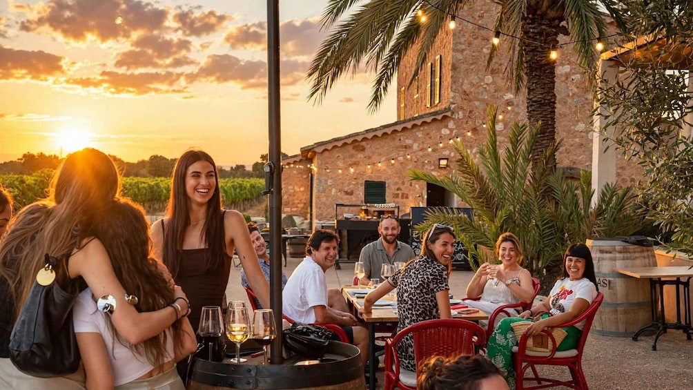 A group of people dining outdoors at sunset with a stone building and string lights in the background. 2
