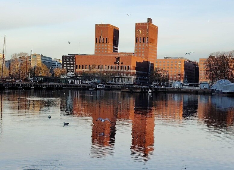 Tyyni joki, jonka pinnasta heijastuvat rakennukset, mukaan lukien huomiota herättävä punatiilinen rakennus, jossa on kellotorni. 3