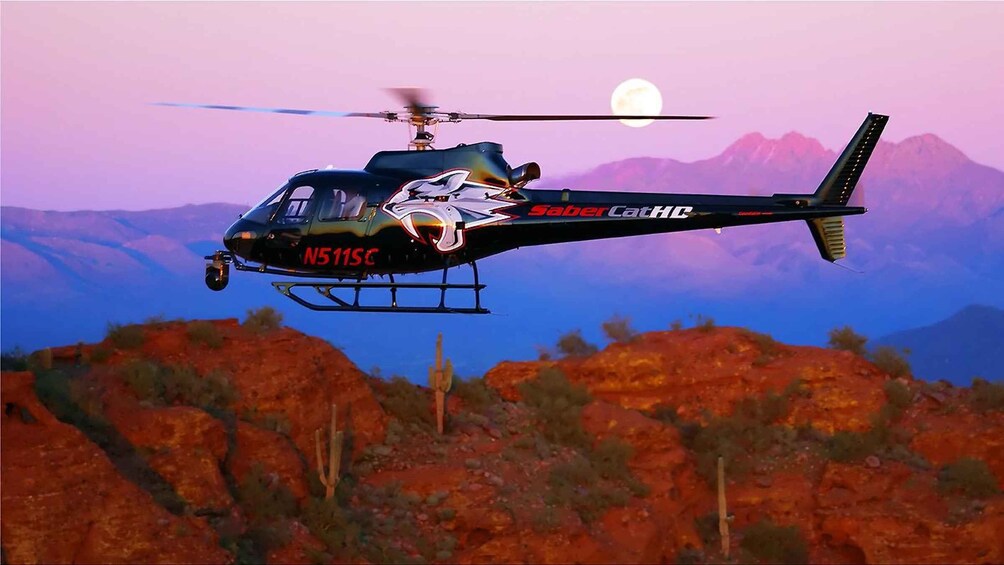 A helicopter with 'Sabercat HC' and 'N511SC' markings flying over a desert landscape with mountains in the background. 1