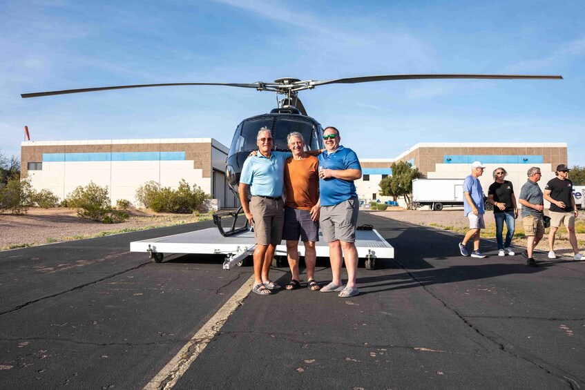 A group of people standing in front of a helicopter on a tarmac with buildings in the background. 2