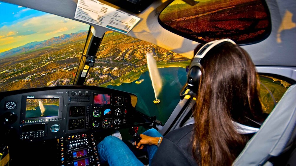 A helicopter cockpit with a view of a coastal landscape, including a body of water and a town below. 4