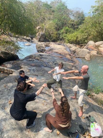 A group of people sitting on rocks by a river, some reaching out towards the water. 3