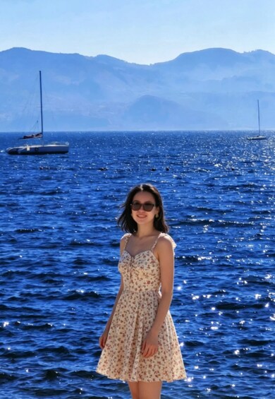 A person standing by a body of water with sailboats and mountains in the background. 4