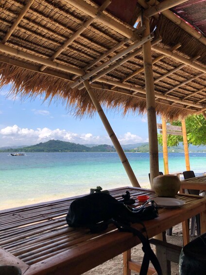 A beachside hut with a thatched roof overlooking turquoise waters and a distant island. 2