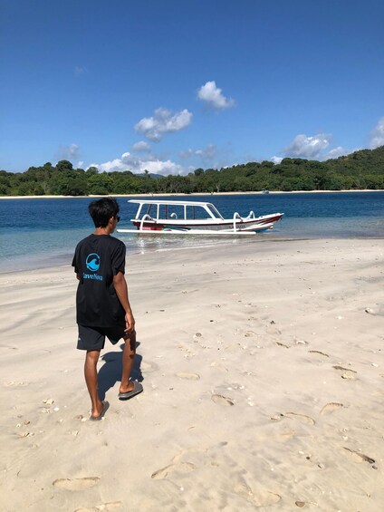 A person walking on a sandy beach with a boat named 'SABARA' in the water. 4