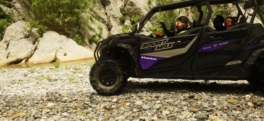 A SportMax ATV on a rocky terrain with a rocky cliff and greenery in the background. 3