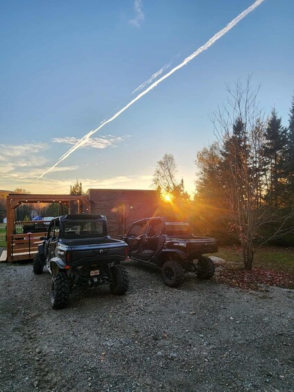 A black off-road vehicle parked on gravel, a wooden structure, and a sunset in the background. 2