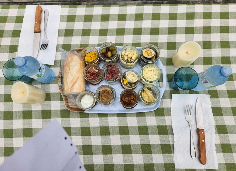 A checkered tablecloth with a tray of food items, including bread, pickles, and various spreads, and utensils on a picnic table. 3