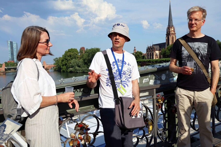 Three people standing by a river with a bridge and a church in the background. 5