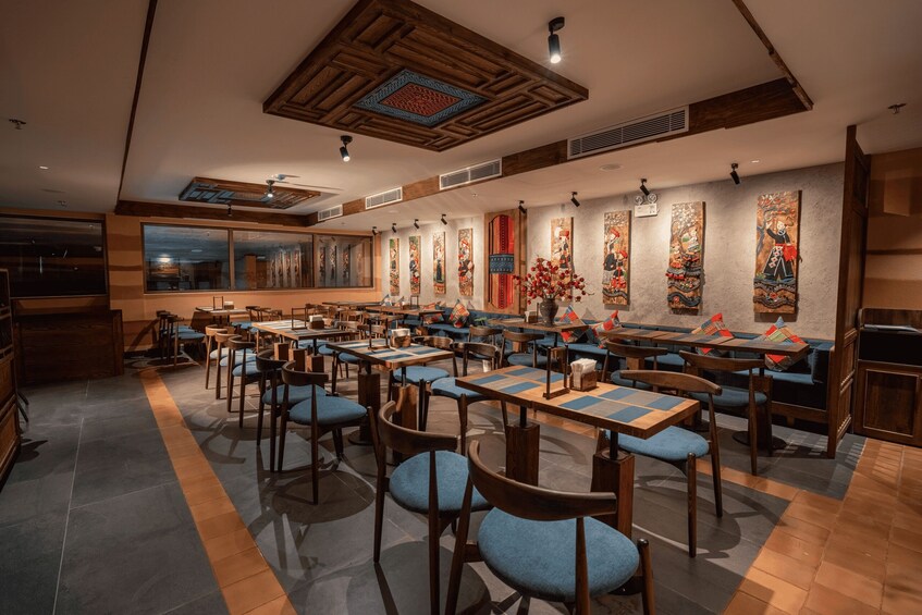 A restaurant interior with wooden tables, blue chairs, and traditional wall art. 2