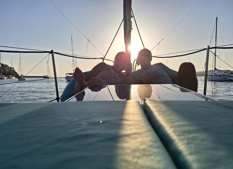 A sunset over a calm sea with sailboats and a person relaxing on a boat. 3