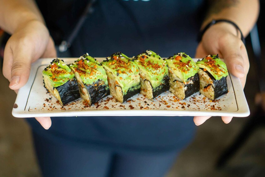 A person holding a plate with sushi rolls topped with avocado and sesame seeds. 4