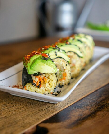 A sushi roll with avocado and sesame seeds on a white plate. 3