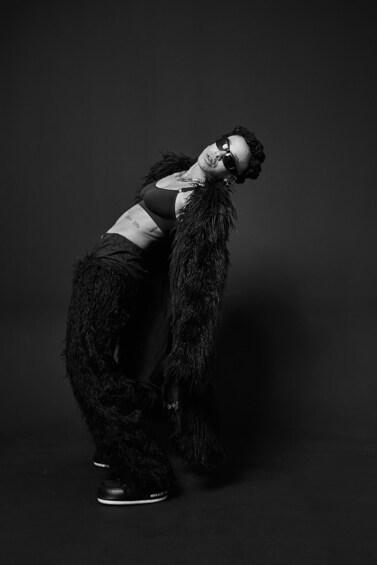 A person in a black furry outfit with a feathered collar, black shoes, and a visible tattoo on the arm. 5