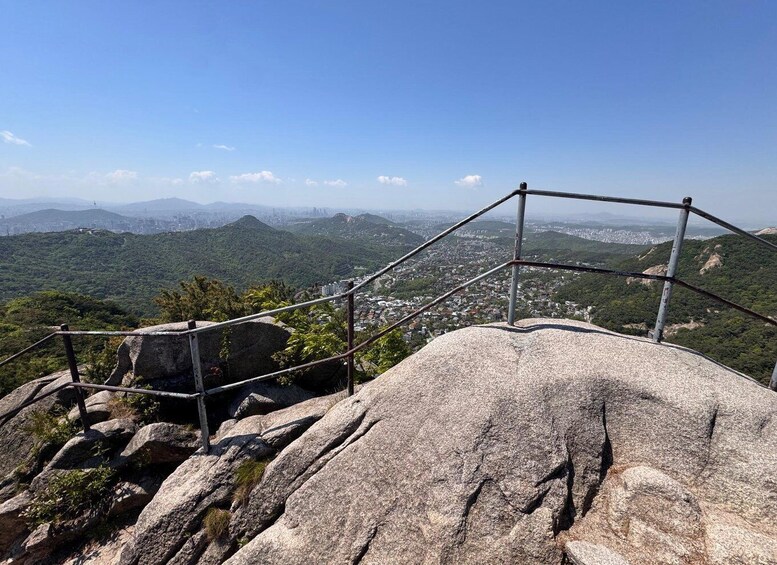 A rocky outcrop with a metal railing overlooking a cityscape. 5