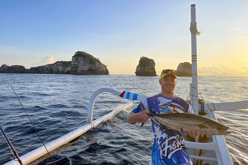 A person on a boat holding a fish, with rocky cliffs in the background. 1