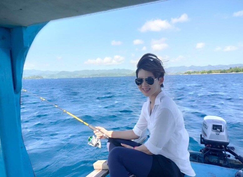 A person fishing on a boat with a clear view of the ocean and distant mountains. 3