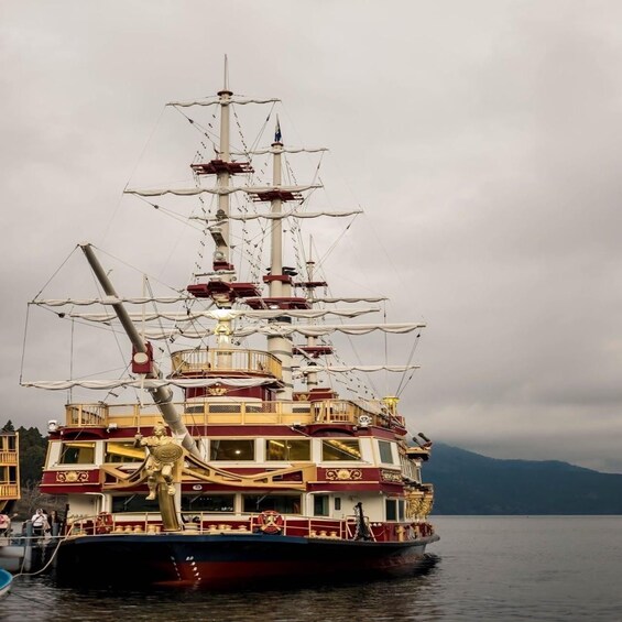 A large, ornate ship with multiple decks and a tall mast, docked at a harbor with mountains in the background. 5