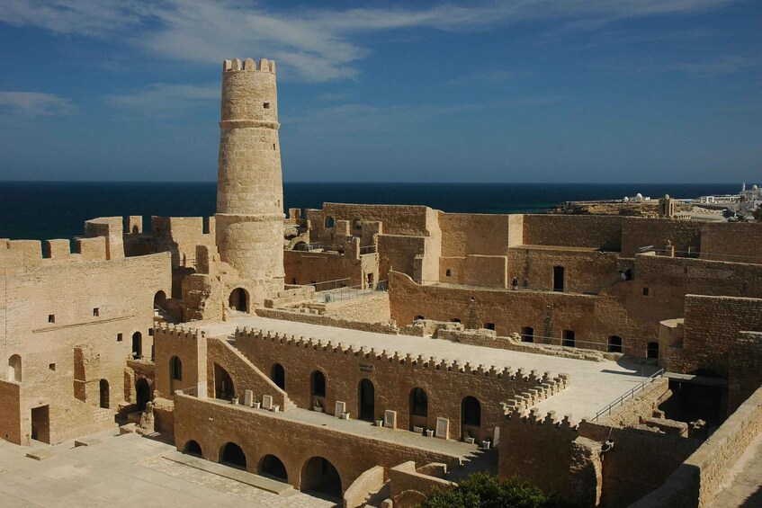 A historical fortification with a prominent tower, arched walkways, and a view of the sea. 5