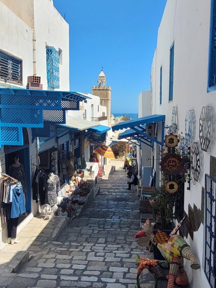 A narrow street with shops and a tower in the background. 4