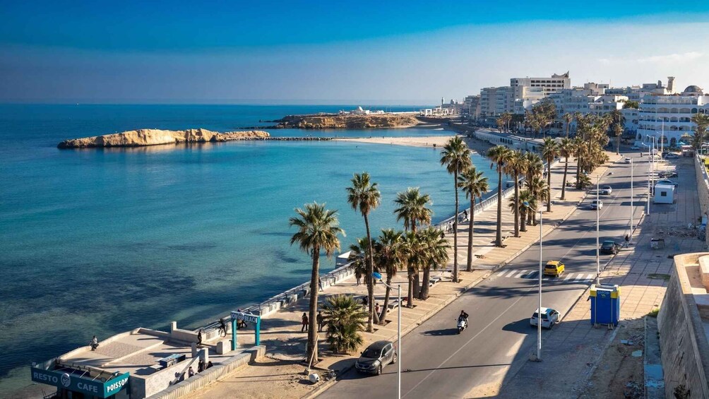 A coastal cityscape with a beach, palm trees, and a clear blue sky. 1