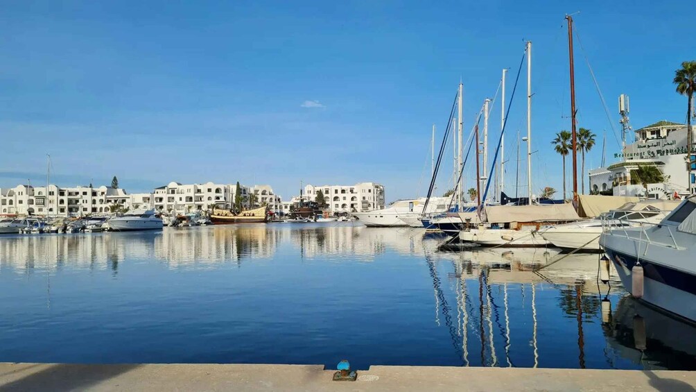 A marina with yachts and sailboats docked, surrounded by white buildings and palm trees. 3
