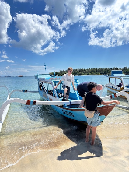 A boat named 'TENANG' with passengers disembarking onto a sandy beach. 2