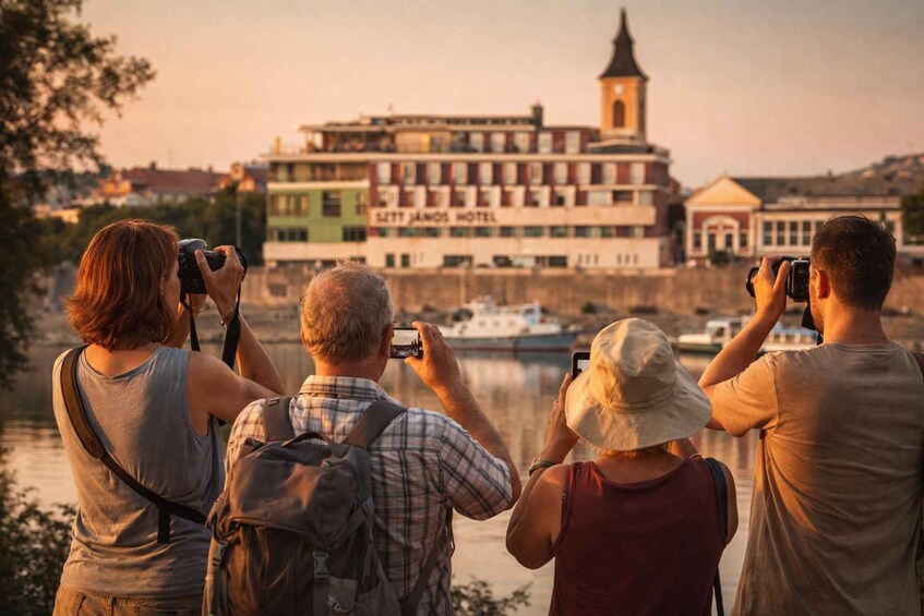 Four people taking photographs of a historic building with a tower, a river, and boats in the foreground. 2