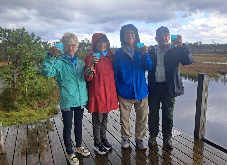 A group of people standing on a wooden dock by a body of water, holding cards. 2